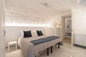 Un dormitorio con cama, mesita de noche, lámpara y vistas al baño.