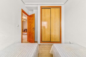 A room with two beds, a wooden wardrobe, and a door leading to another room.