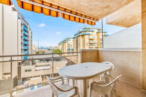 A balcony with a table and chairs, overlooking a residential area with multiple buildings.