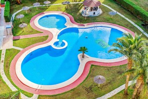 A swimming pool with a unique design, surrounded by a brick pathway and palm trees.