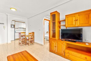A living room with a wooden entertainment unit, a flat-screen TV, and a dining area with chairs and a table.