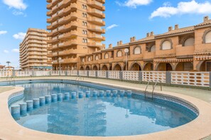 A swimming pool with a tiled edge, surrounded by a building with multiple balconies and arched windows.