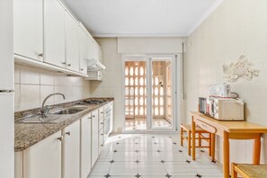 Une cuisine avec des meubles blancs, un plan de travail en granit, un évier, un four à micro-ondes et une table en bois.