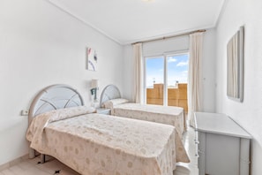 Une chambre avec deux lits, une table de chevet, un miroir et une fenêtre avec des rideaux.
