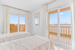 A hotel room with two beds, large windows, a balcony, and a view of the cityscape.