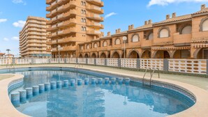 A swimming pool with a tiled edge, surrounded by a building with multiple balconies and arched windows.