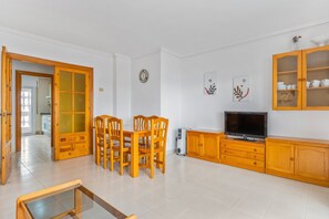 Un coin repas comprenant une table et des chaises en bois, un téléviseur et un meuble avec des portes en verre.