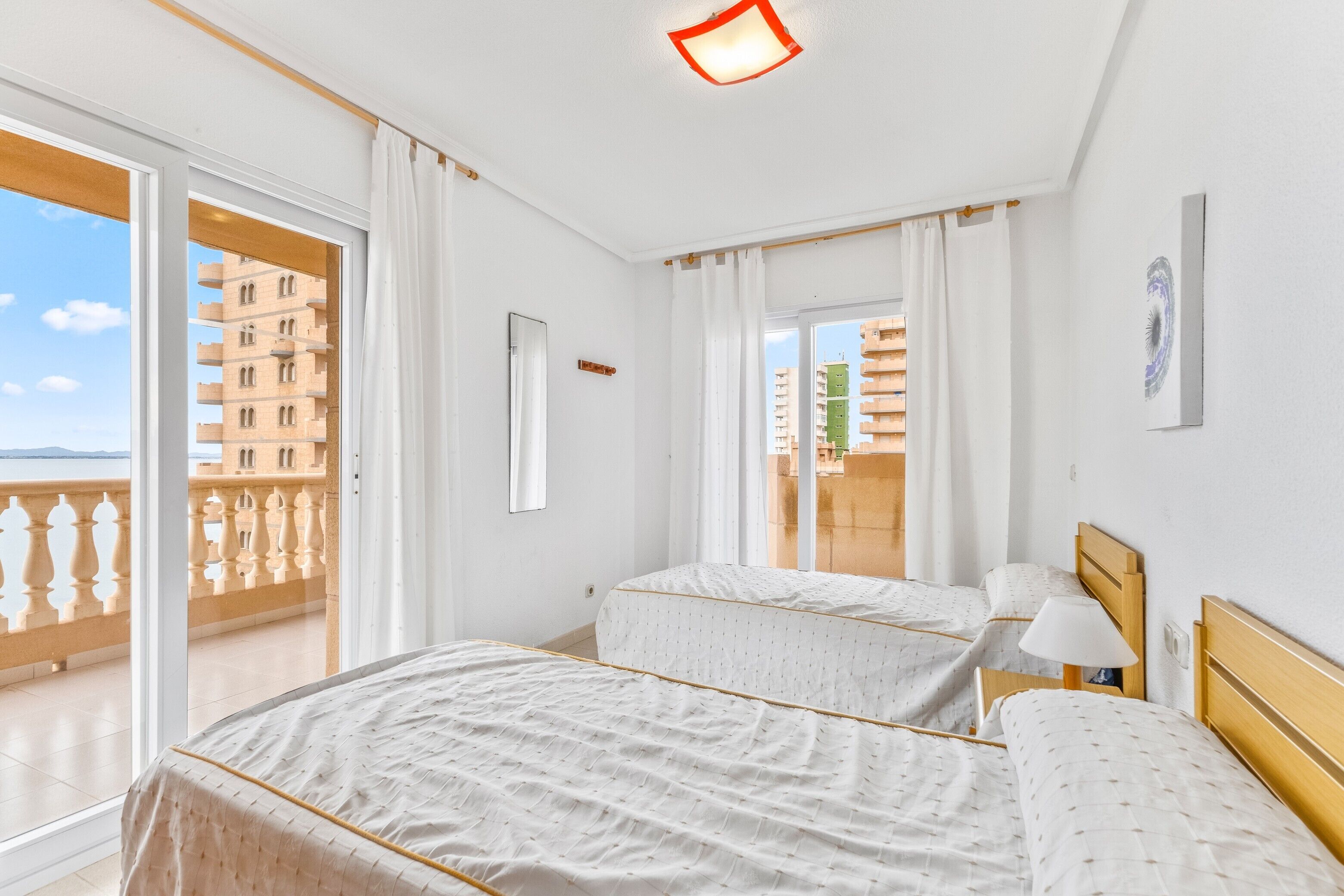 Een hotelkamer met twee bedden, een balkon en uitzicht op gebouwen.