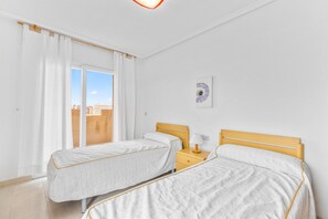 Une chambre avec deux lits, une fenêtre avec des rideaux, une table de chevet avec une lampe et une œuvre d’art accrochée au mur.