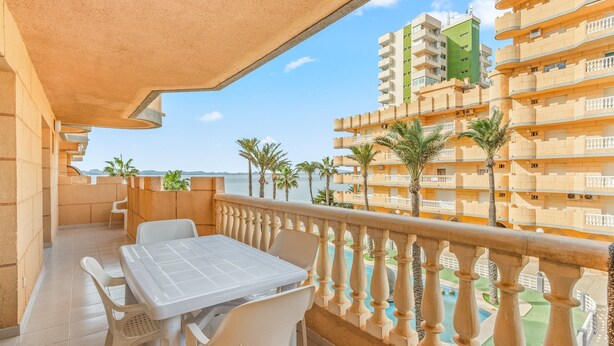 A balcony with a table and chairs, overlooking a pool and adjacent buildings. - Apartment 'Castillo De Mar F3 Torre Sur 2a' with Sea View, Shared Pool and Wi-Fi (La Manga del Mar Menor)