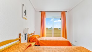 A room with two beds, a wooden headboard, a wall-mounted lamp, and a window with orange curtains. - Apartment 'Castillo De Mar F3 Torre Sur 2a' with Sea View, Shared Pool and Wi-Fi (La Manga del Mar Menor)
