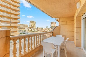 A balcony with a white table and chairs, a balustrade, and a view of high-rise buildings and palm trees.