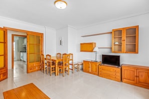 Un ampio soggiorno con zona pranzo, mobili in legno, televisione e cucina visibile attraverso una porta aperta.
