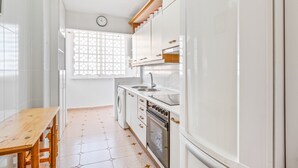 A kitchen with white cabinets, a wooden table, a washing machine, and a clock on the wall.