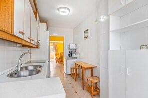 Keittiössä on pesuallas, puiset jakkarat, pöytä ja valkoiset kaapit.