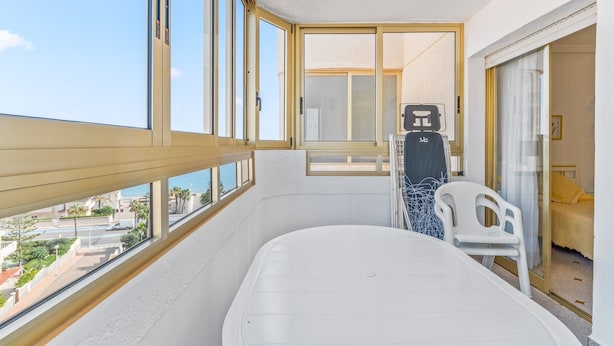 A balcony with a view of the city, a white chair, and a bed with a yellow pillow.