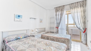 A bedroom with two beds, a nightstand, a lamp, a window with curtains, and a view of the outside.