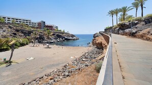 Une route côtière bordée d’une plage, d’un terrain rocheux, de palmiers et d’un immeuble à plusieurs étages.