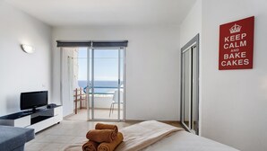 Une chambre d’hôtel avec un lit, une télévision, une vue sur la mer et une pancarte indiquant : « Restez calme et préparez des gâteaux ».