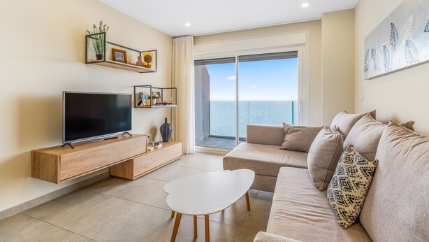 A modern living room with a flat-screen TV, a sofa, a coffee table, and a large window offering a view of the sea. - Apartment 'Playa Principe Esc 10' with Sea View, Wi-Fi and Air Conditioning (La Manga del Mar Menor)
