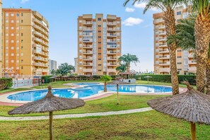Un hôtel doté d’une piscine, de palmiers et dont l’arrière-plan est constitué d’immeubles de grande hauteur.