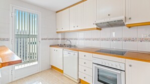 Eine Küche mit weißen Schränken, einem Geschirrspüler, einem Backofen und einem Fenster mit Jalousien.