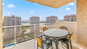 Ein Balkon mit rundem Tisch und Stühlen, Blick auf andere Gebäude und einen klaren Himmel.