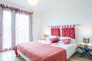 Un dormitorio con cama, cortinas, mesita de noche y lámpara.