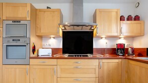 A kitchen with wooden cabinets, a built-in oven, a stove, and a coffee maker. - Holiday Home 'Maison Vue Mer 150m De La Plage' with Sea View, Private Terrace and Wi-Fi (Trégunc)