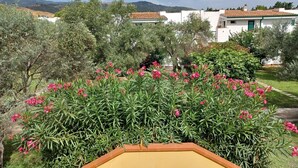 A residential area with white houses, a garden with pink flowers, and a hilly landscape in the background.
