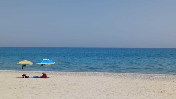 A beach with two umbrellas and a person lying on the sand.