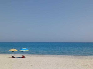 A beach with two umbrellas and a person lying on the sand. - Apartment 'Tra Ulivi e Mare' in Villaggio Sant'Andrea (Sant'Andrea Apostolo dello Ionio)