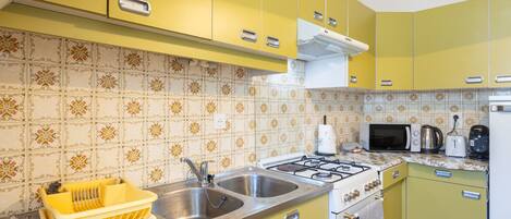 Een keuken met gele kastjes, een gasfornuis, een spoelbak en een magnetron.