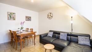 A living room with a black leather sofa, wooden dining table, chairs, and a small stool. - Holiday Apartment "Gîte Le Lot " with Wi-Fi (ESPALION)