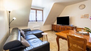 A living room with a sofa, a dining table with chairs, a television, and a window with curtains. - Holiday Apartment "Gîte Le Lot " with Wi-Fi (ESPALION)