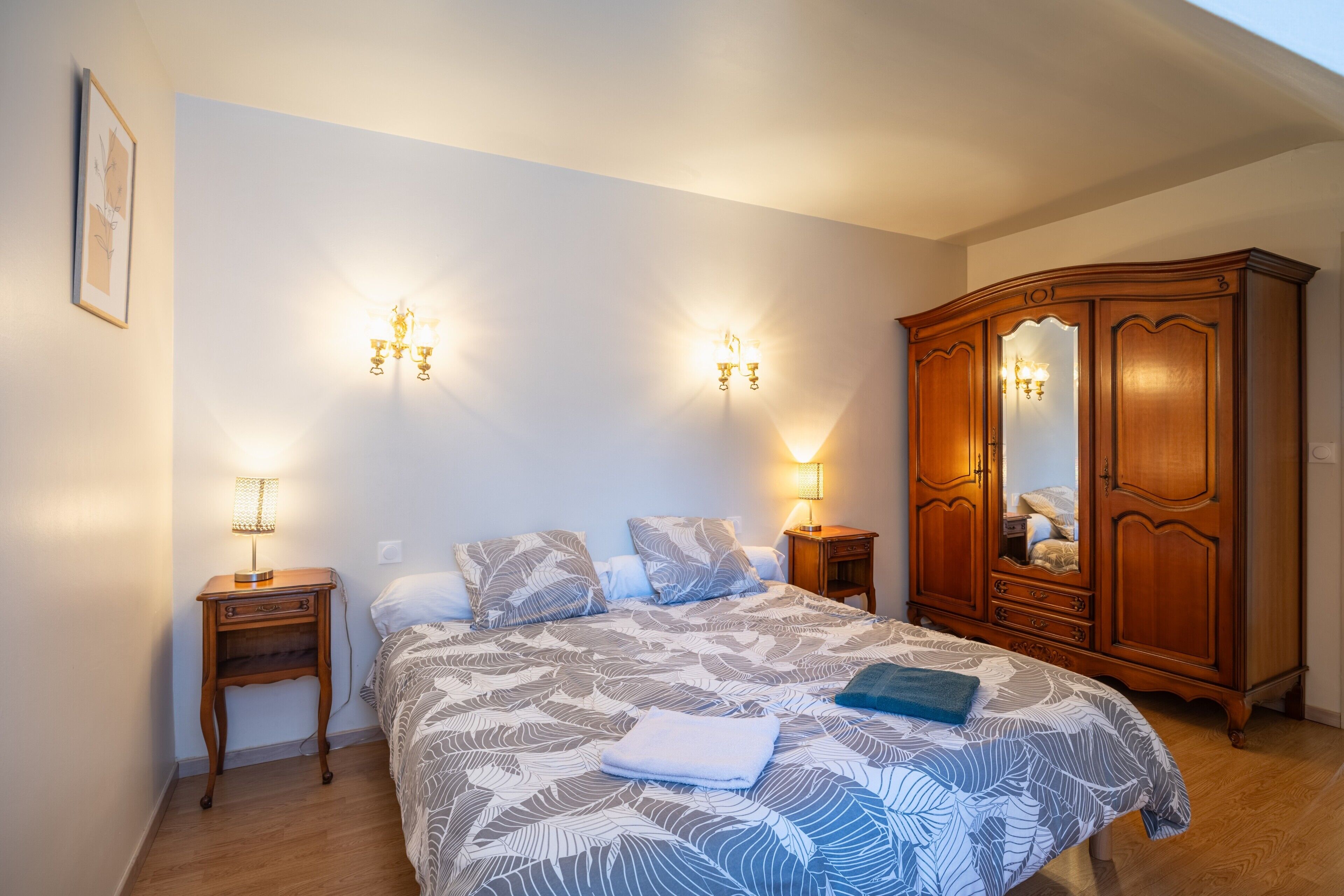 Een slaapkamer met een bed, twee nachtkastjes, een garderobe en wandlampen.