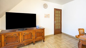 A living room with a flat-screen TV on a wooden cabinet, a clock on the wall, and a wooden door. - Holiday Apartment "Gîte Le Lot " with Wi-Fi (ESPALION)