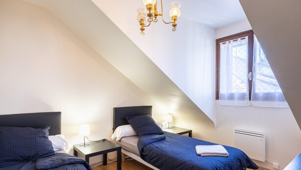 A bedroom with two beds, a chandelier, a window with curtains, and a radiator. - Holiday Apartment "Gîte Le Lot " with Wi-Fi (ESPALION)