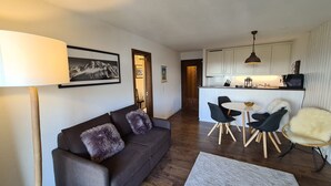 A modern living room with a sofa, a dining table with chairs, and a kitchen area with cabinets and a microwave. - Greppons N 012 - MOUNTAIN apartment 6 pers (Veysonnaz)