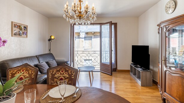 Ein Wohnzimmer mit einer Deckenleuchte, einem Essplatz, einer Couch, einem Fernseher und einem Balkon.