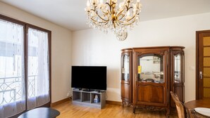 Ein Wohnzimmer mit Flachbildfernseher, Holzschrank, einer Kandelaberleuchte und einem Esstisch.