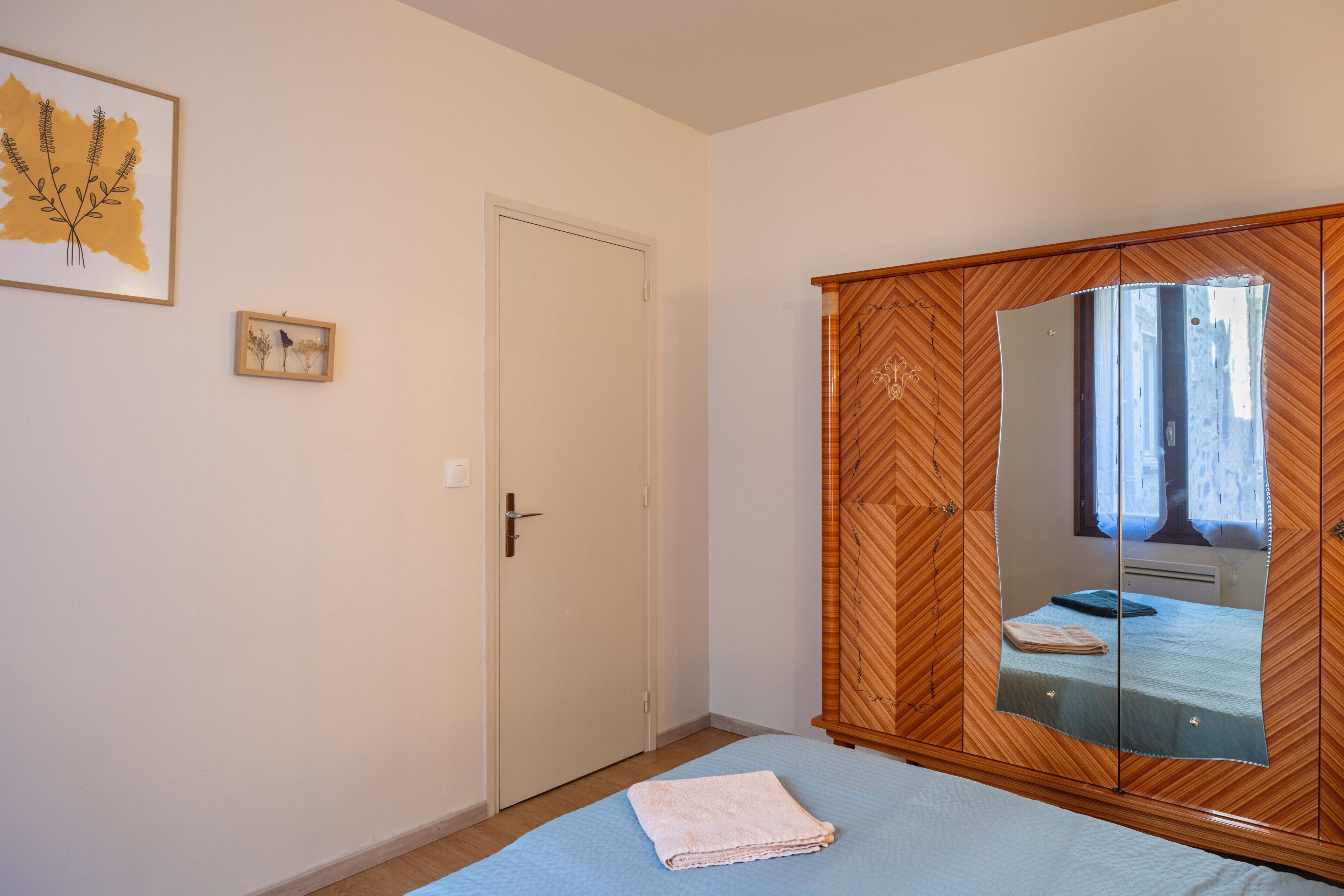 Een slaapkamer met een bed, een kledingkast, een deur en een kunstwerk aan de muur.