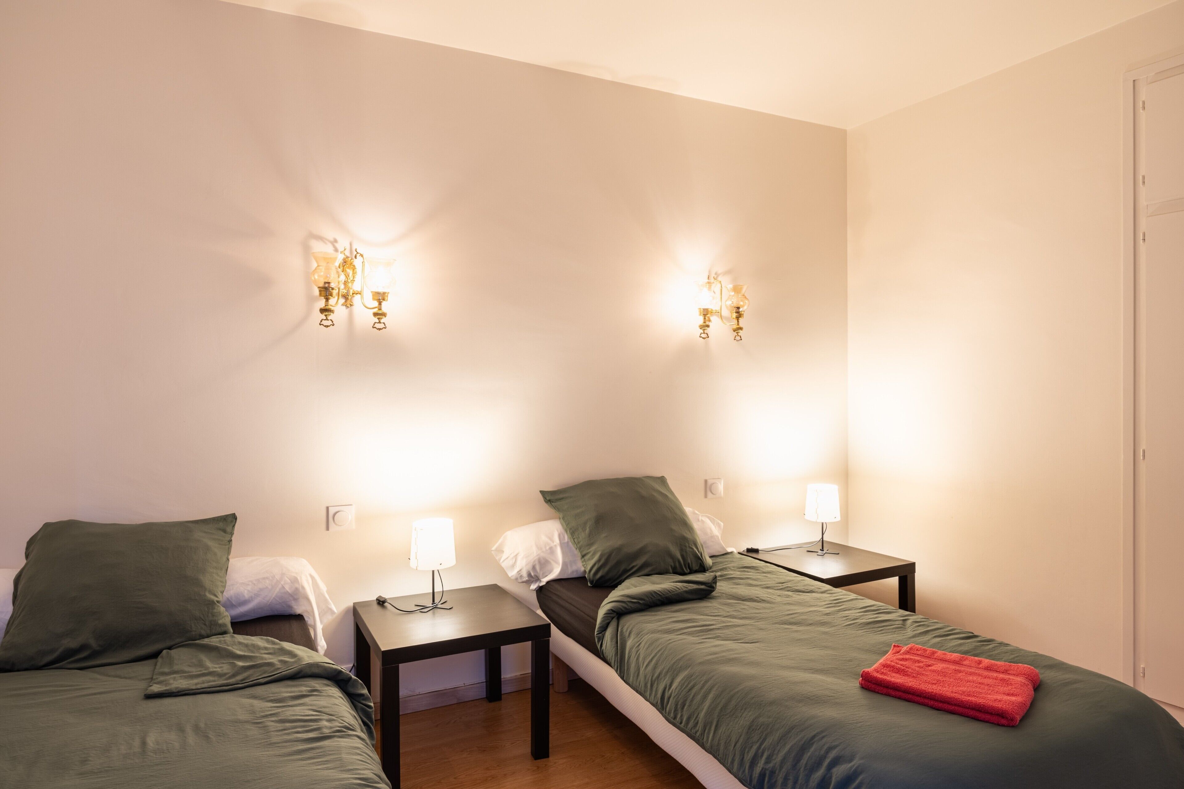 Une chambre d’hôtel avec deux lits, deux tables de chevet, des appliques murales et une porte.