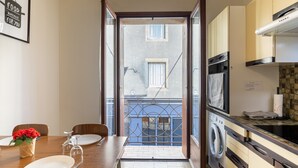 Une cuisine équipée d’un lave-linge, d’une table à manger avec des chaises, et offrant une vue sur l’extérieur grâce à une porte ouverte.
