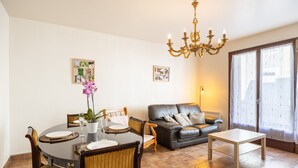 Un coin repas avec une table ronde, des chaises et un lustre. On y trouve également un canapé et une fenêtre avec des rideaux.