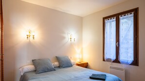 Une chambre à coucher comprenant un lit, deux lampes fixées au mur, une table de chevet, une fenêtre avec des rideaux et un radiateur.