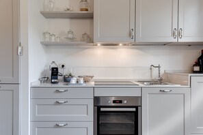 Una cucina moderna con mobili bianchi, forno integrato, macchina da caffè e lavello.