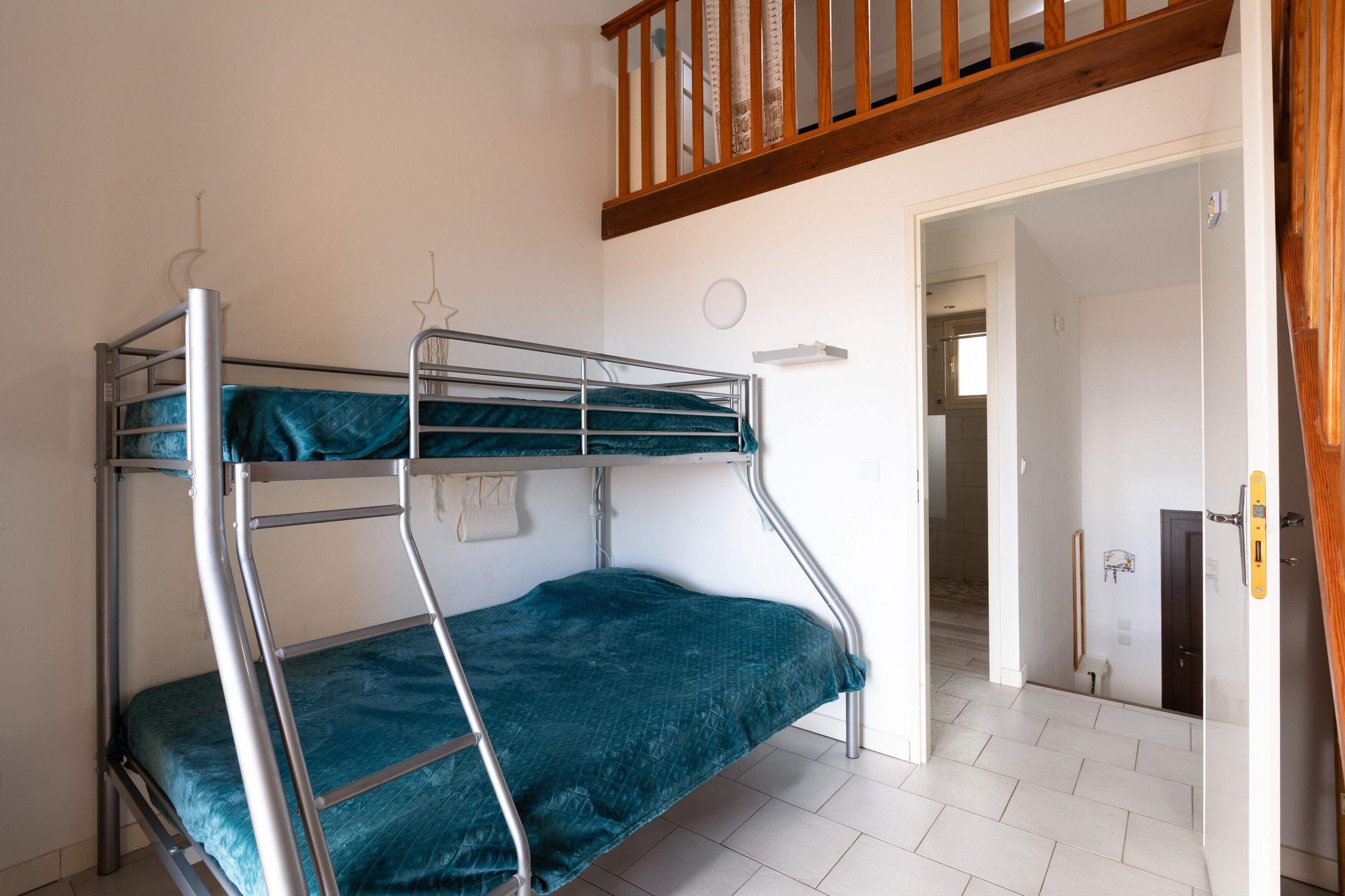 A bunk bed with a metal frame and teal bedding, a wooden staircase, and a white tiled floor.