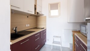 A compact kitchen with a sink, cabinets, a microwave, and a small stool.