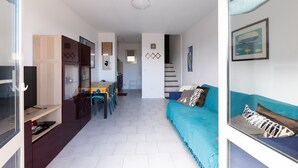 A modern living room with a sofa, a dining area with chairs and a table, and a staircase leading to another level.